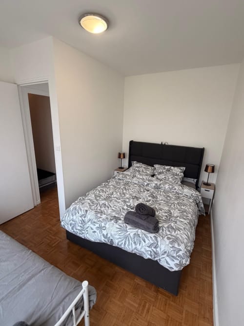 Chambre moderne avec lit noir, linge de lit à motifs et parquet à l'appartement Kawichimmo Locations à Louvres