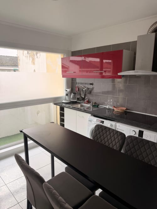 Cuisine moderne dans un appartement 2 chambres à Kawichimmo Locations, Louvres, avec armoires rouges, plan de travail noir et coin repas