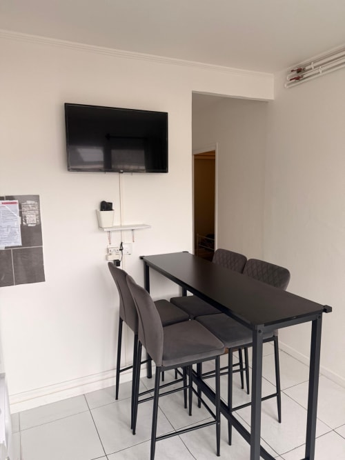 Espace de réunion moderne à l'appartement Kawichimmo Locations à Louvres avec table noire, chaises grises, TV murale