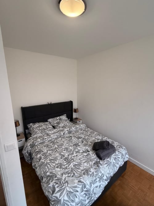 Chambre moderne de l'appartement Kawichimmo Locations, avec stores, lit à cadre noir, linge de lit à motifs, parquet et plafond