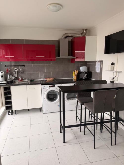 Cuisine-salle à manger moderne aux Locations Kawichimmo à Louvres : meubles rouges, bar petit-déjeuner et électroménagers