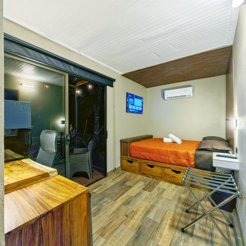 Habitación de hotel en contenedor moderno con cama naranja, escritorio de madera, TV, aire acondicionado y puerta de cristal en Contenedores Boutique