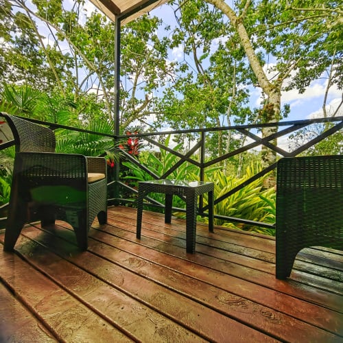 Terraza de madera con sillas de mimbre negro con vista a exuberantes jardines tropicales en Contenedores Boutique Hotel, Costa Rica