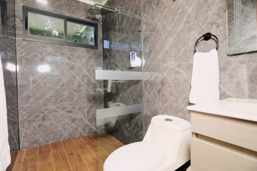 Baño moderno del Contenedores Boutique Hotel con ducha de mármol, inodoro blanco y piso de madera