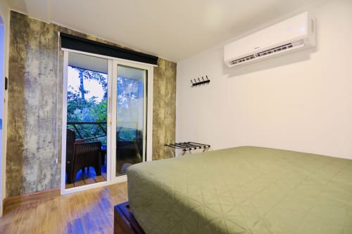 Dormitorio de villa moderna con cama verde, aire acondicionado y puertas de cristal hacia balcón con vista al jardín en Contenedores Boutique Hotel