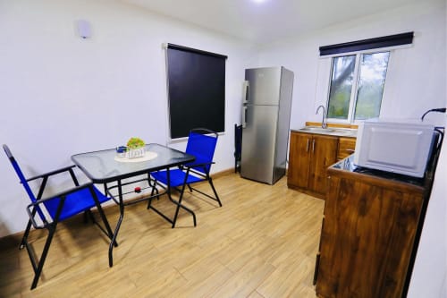 Elegante sala de estar con comedor, sillas azules, cocina, refrigerador, TV y vista al jardín en Contenedores Boutique