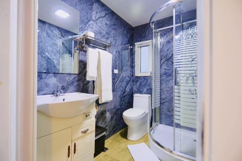 Baño moderno con paredes de mármol azul, ducha de lluvia, lavamanos blanco y sanitario en la villa del Contenedores Boutique Hotel