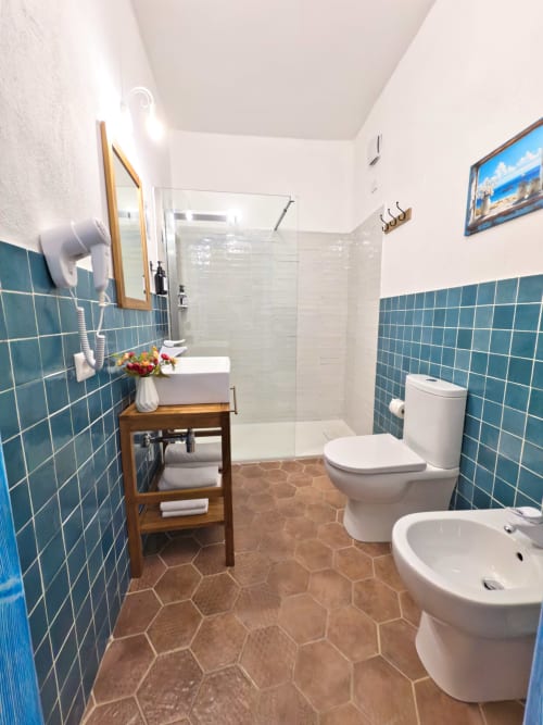 Bagno moderno con piastrelle turchesi, doccia a filo, doppio lavabo e bidet presso le Regnos Altos Boutique Rooms a Bosa