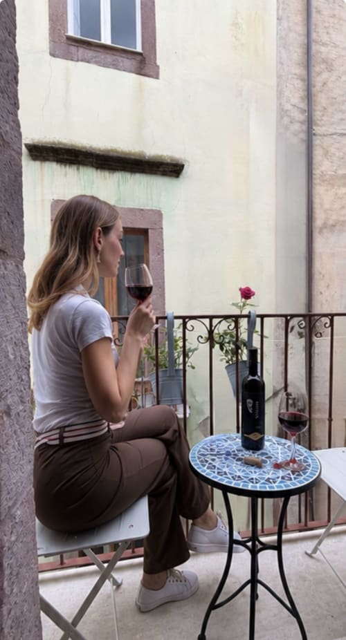 Donna che gusta un vino rosso sul balcone di Regnos Altos Boutique Rooms a Bosa, con rosa e vista sulla città