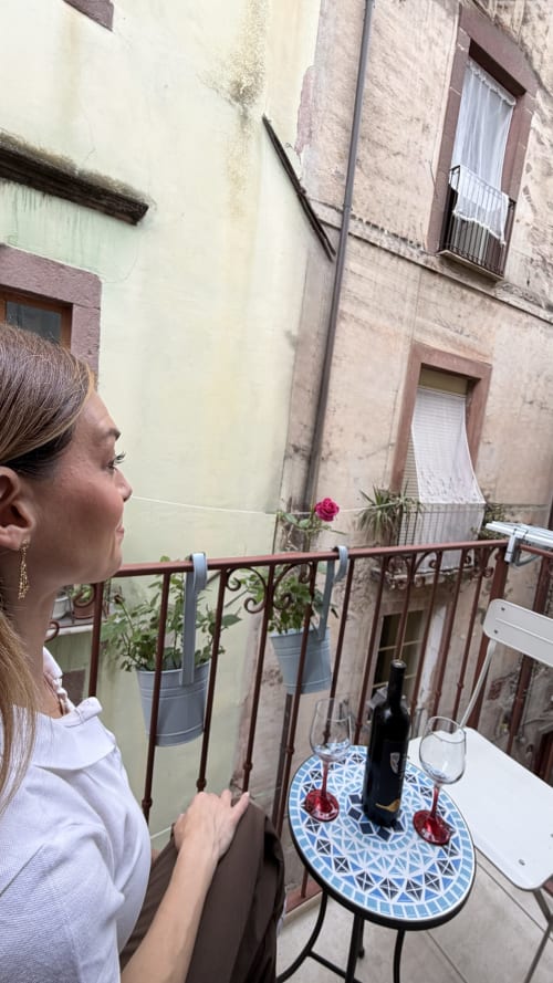 Donna al balcone con vista sul cortile di Bosa presso le Regnos Altos Boutique Rooms, con vino e fiori in vaso