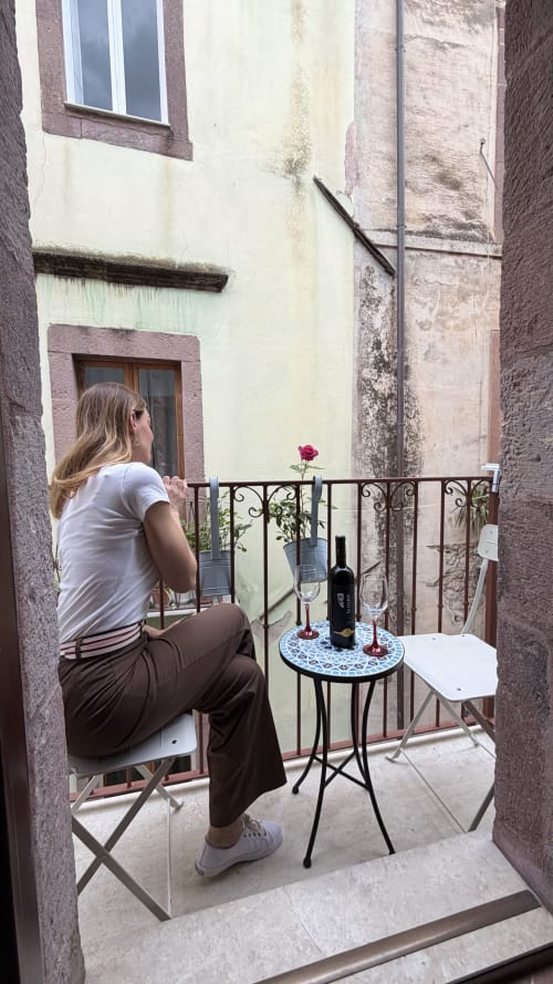 Donna che assapora vino su un balcone stretto con rosa rossa presso Regnos Altos Boutique Rooms a Bosa, Italia