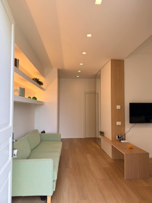 Modern hotel room at Adagio Ravello with green sofa, built-in shelving, wooden desk, flat-screen TV, and garden views in