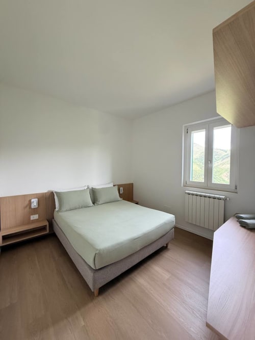 Modern bedroom at Adagio Ravello with double bed, wood nightstand, large window overlooking garden, radiator heating, and