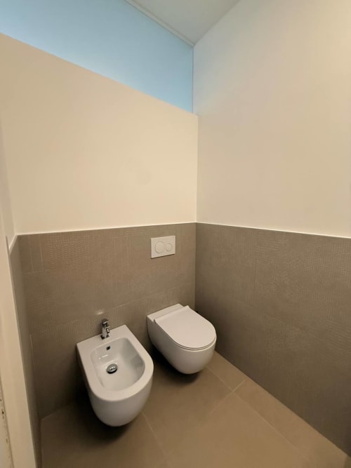 Modern bathroom in Adagio Ravello hotel room with white bidet and toilet, beige textured tiles, and light upper walls