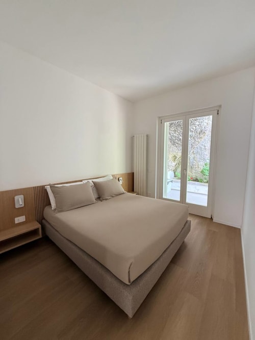 Modern bedroom at Adagio Ravello with beige bedding, wood headboard, garden view doors, and minimalist decor