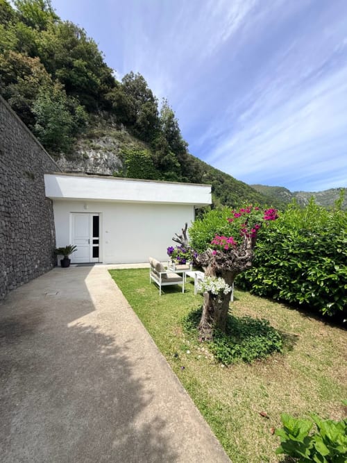 Modern white bungalow with garden seating at Adagio Ravello, featuring pink flowers and mountain views in Ravello, Italy