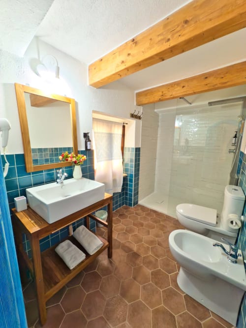 Bagno spazioso a Regnos Altos Boutique Rooms a Bosa con travi in legno, dettagli in piastrelle blu, lavabo su piedistallo e doccia walk-in