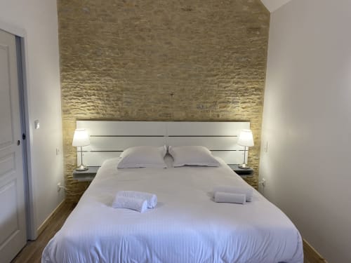 Modern studio bedroom at Domaine des Piéris with textured stone accent wall, white bedding, integrated lighting, and wooden