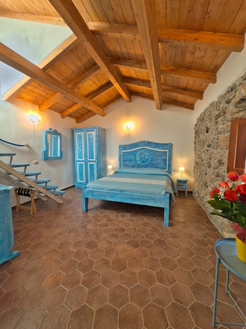 Letto in legno blu nella camera rustica di Regnos Altos Boutique Rooms a Bosa, con travi a vista e muri in pietra