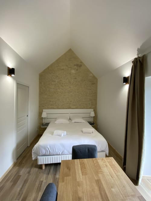 Modern studio bedroom at Domaine des Piérs, Grandcamp-Maisy with white bed, brick accent wall, and wooden desk