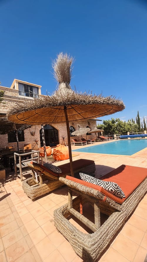 Maison la Chèvre poolside lounge with thatched umbrella, woven seating, and blue pool in Essaouira