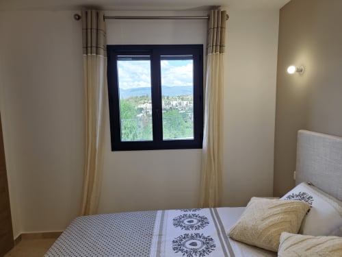 Bright bedroom at Smooth Luberon with French mountain and village views through black-framed windows, beige curtains, and