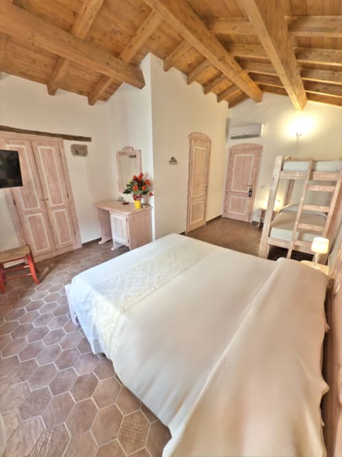 Camera spaziosa a Regnos Altos Boutique Rooms a Bosa con letto, travi in legno a vista, mattonelle in cotto e legno rosa