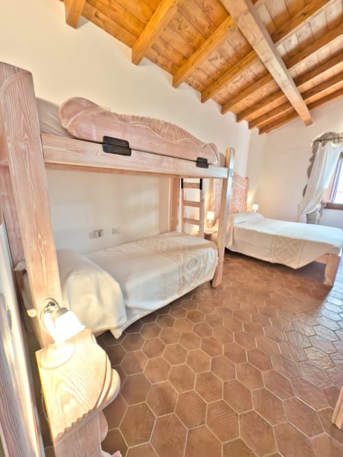Camera da letto rustica con letti a castello in legno, piastrelle esagonali in cotto e soffitto con travi a vista presso Regnos Altos a Bosa