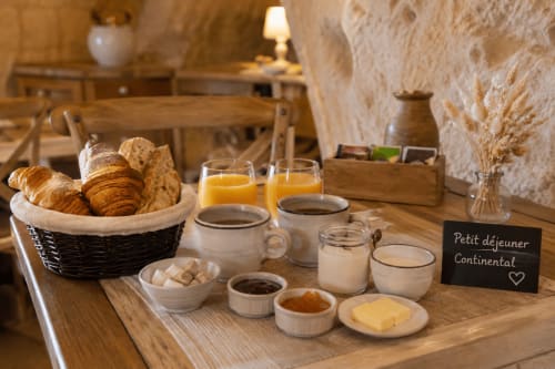 Continental breakfast spread at Les Troglos de Beaulieu featuring croissants, bread, coffee, juice, butter and jam in rustic