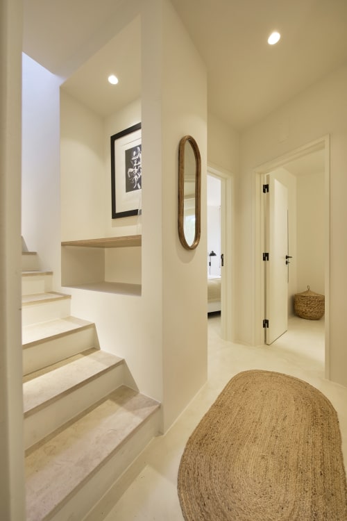 Modern hallway in Casa Redonda apartment at Aroeira resort with white walls, floating stairs, oval mirror, and woven baskets