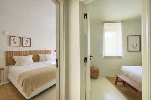Two bright bedroom views at Casa Redonda in Aroeira showing beds with neutral bedding, wooden headboards, and botanical