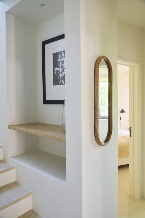 Modern hallway with white shelving, wooden shelf detail, framed black artwork, oval mirror with wooden frame, and