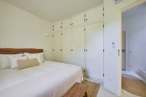 Bright bedroom in Casa Redonda apartment at Aroeira with wooden bed, cream wardrobe, and ensuite bathroom view