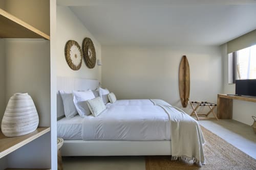 Quarto moderno e luminoso na Casa Redonda em Aroeira com roupa de cama branca, arte têxtil artesanal na parede e vista para o jardim