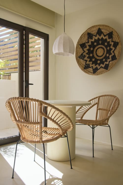 Sala de jantar minimalista com cadeiras de rattan trançado, mesa redonda e cesto decorativo na Casa Redonda, Aroeira