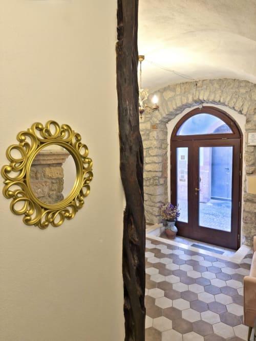 Specchio dorato ornamentale su parete color crema con trave in legno scuro nella Suite Regnos Altos, Bosa Italia