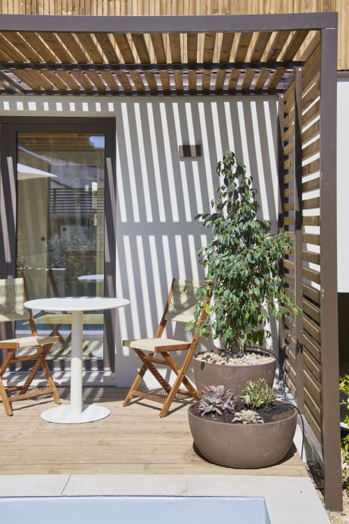Modern patio at Casa Redonda with wooden pergola, dining table, potted plants, and striped privacy screen at Aroeira villa