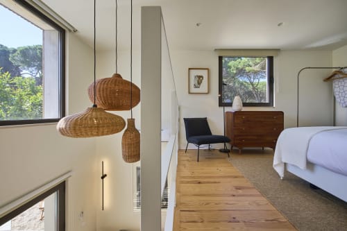 Modern bedroom at Casa Redonda Aroeira with woven pendant lights, wooden furniture, and large windows overlooking the pool