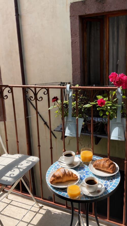 Colazione in balcone a Regnos Altos Bosa con cornetti, caffè, succo d'arancia e fiori rosa con vista sulla città