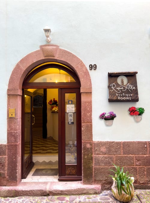 Ingresso di Regnos Altos Boutique Rooms a Bosa, Italia, con porta in legno ad arco, fiori e insegna