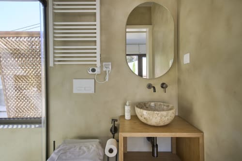 Modern bathroom with stone sink, round mirror, and wooden vanity at Casa Redonda apartment in Aroeira