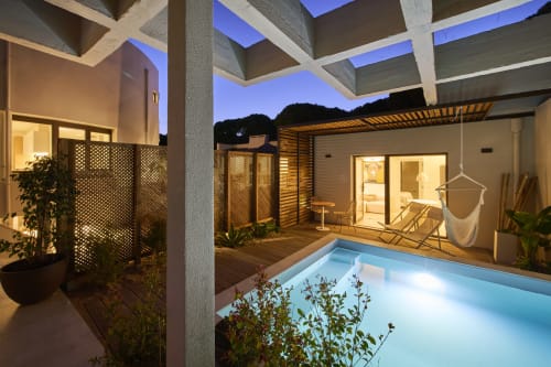 Piscina e jardim da Casa Redonda ao anoitecer, Aroeira. Pátio iluminado com espreguiçadeiras, pérgula e arquitetura moderna.