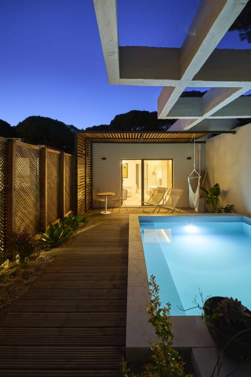 Piscina e jardim da Casa Redonda ao entardecer, Aroeira, Portugal. Apartamento moderno iluminado com espreguiçadeiras, deck de madeira