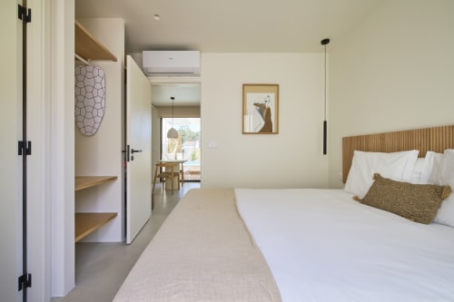 Quarto moderno com vista para a piscina em Casa Redonda, Aroeira. Cabeceira de madeira, roupa de cama branca, iluminação pendente e acesso a