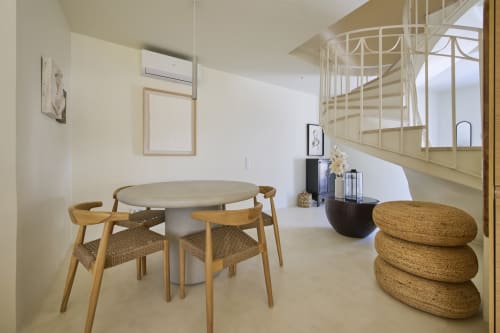 Modern dining area with wooden chairs, round table, spiral staircase, and woven poufs at Casa Redonda, Aroeira Portugal