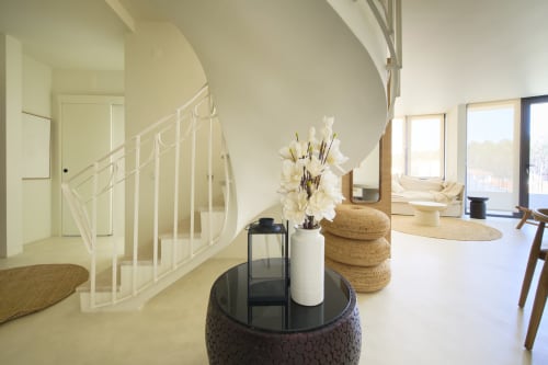 Modern open-plan living area at Casa Redonda, Aroeira with curved staircase, round side table, white flowers, and garden