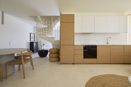 Modern kitchen and living area in Casa Redonda apartment at Aroeira villa with wooden cabinets, spiral staircase, and natural