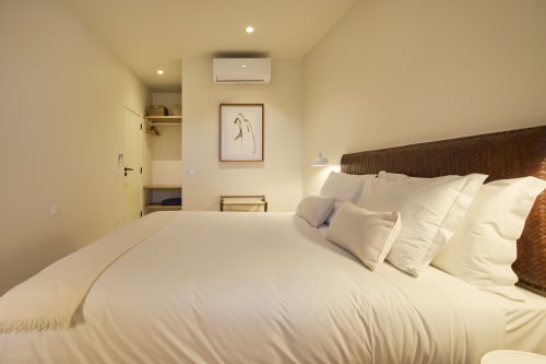 Modern bedroom at Casa Redonda by Villas Aura in Aroeira with white linens, woven headboard, and garden view