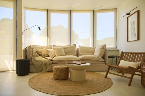 Bright living area at Casa Redonda with beige sofa, wooden chair, and round jute rug overlooking Aroeira pool view