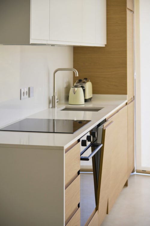 Modern kitchen in Casa Redonda apartment at Aroeira with white cabinets, light wood finishes, and stainless steel appliances